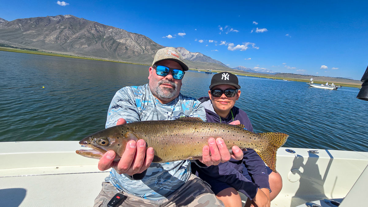 A fly fishermen holding a large cutthroat trout in a boat on Crowley Lake in the Eastern Sierra.