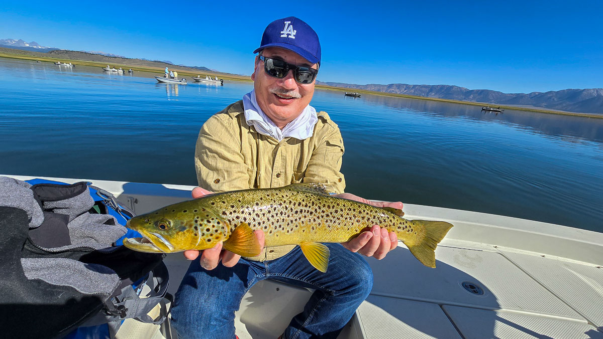 A fly fishermen holding a large brown trout in a boat on Crowley Lake in the Eastern Sierra.