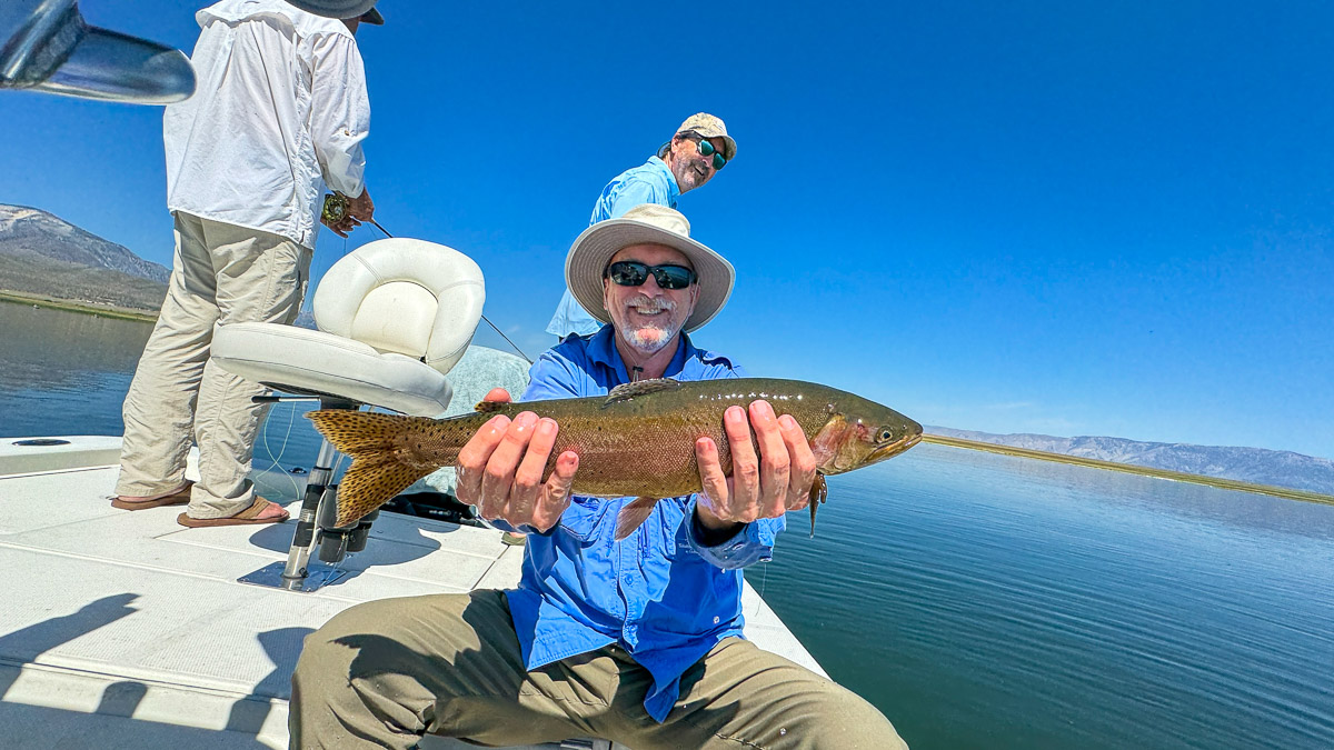 A fly fishermen holding a large cutthroat trout in a boat on Crowley Lake in the Eastern Sierra.