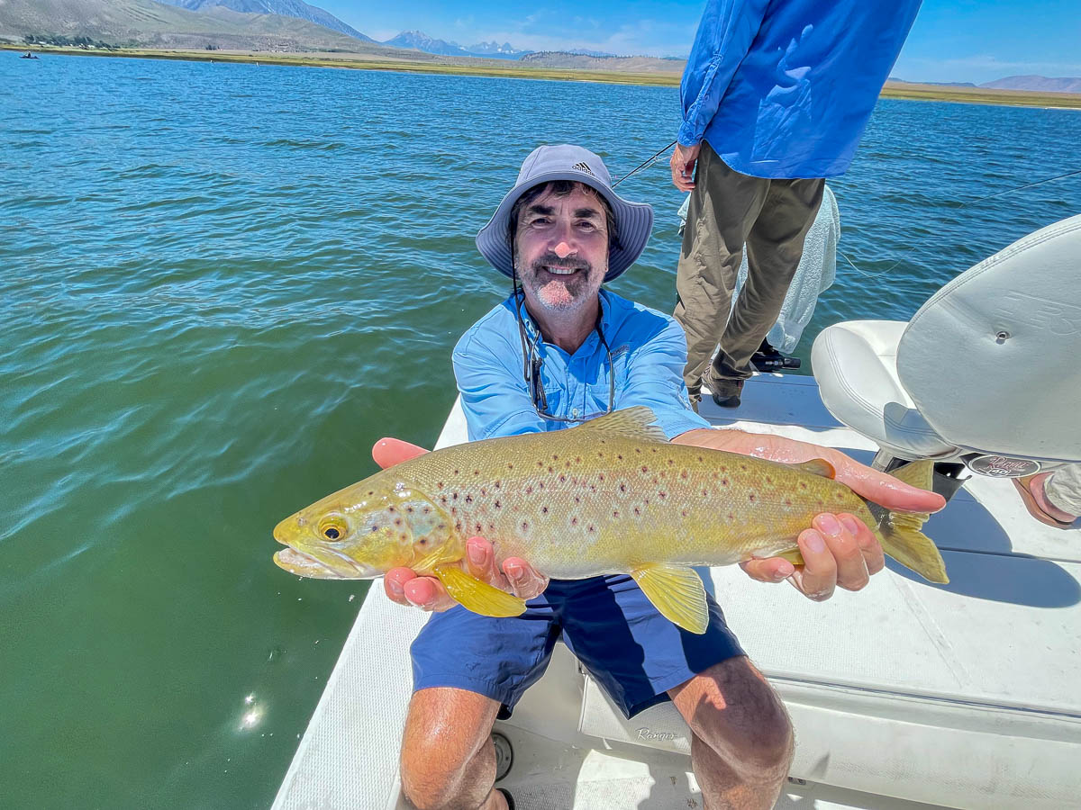 A fly fishermen holding a large brown trout in a boat on Crowley Lake in the Eastern Sierra.