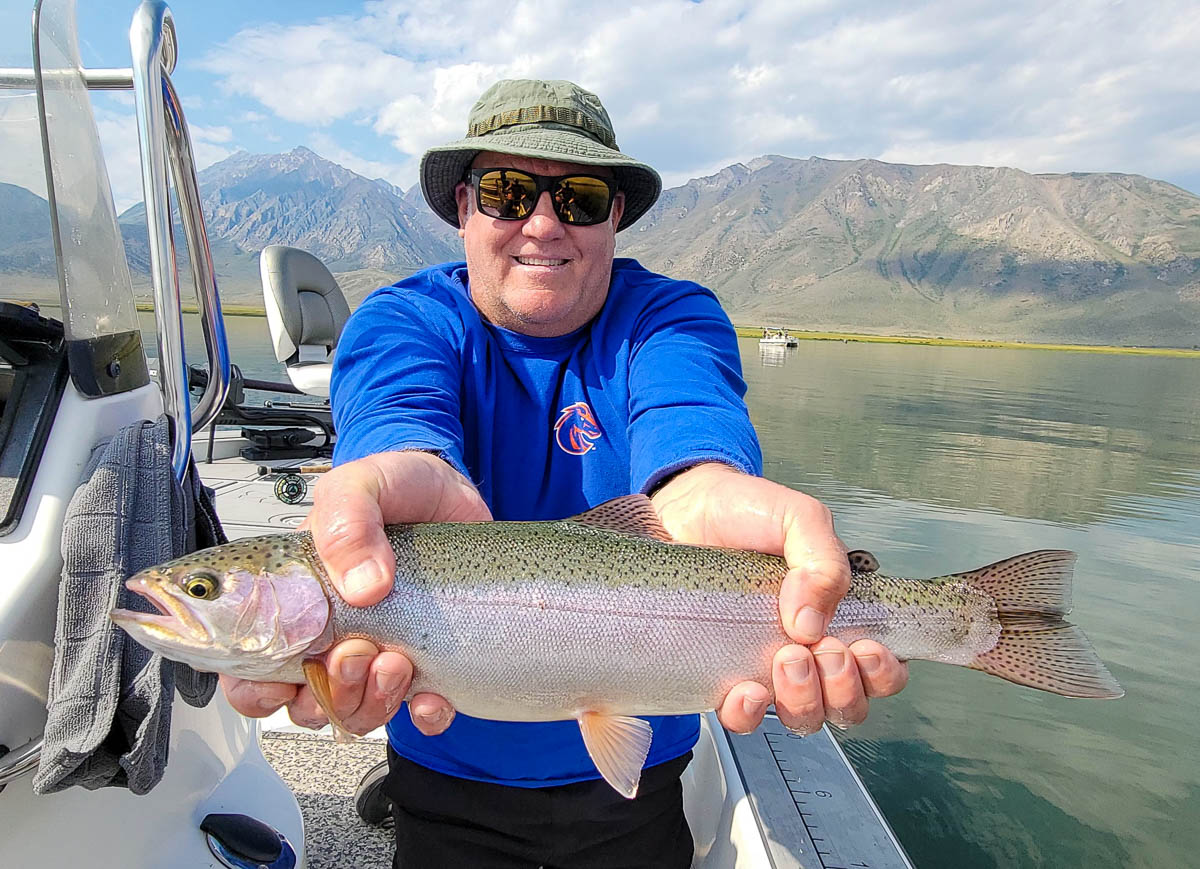 A fly fishermen holding a large rainbow trout in a boat on Crowley Lake in the Eastern Sierra.