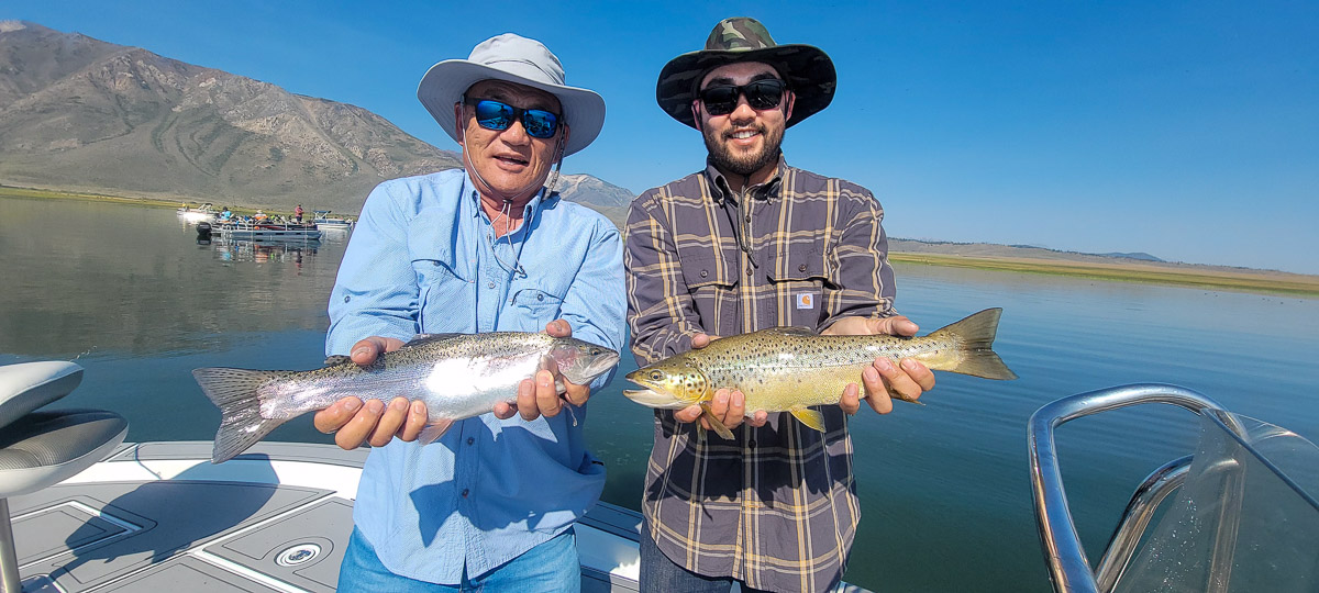 A couple of fly fishermen holding a large rainbow and large brown trout in a boat on Crowley Lake.