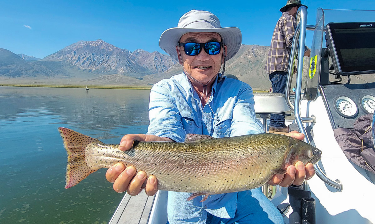 A fly fishermen holding a large cutthroat trout in a boat on Crowley Lake in the Eastern Sierra.