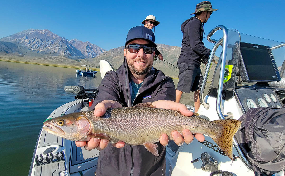 A fly fishermen holding a large cutthroat trout in a boat on Crowley Lake in the Eastern Sierra.