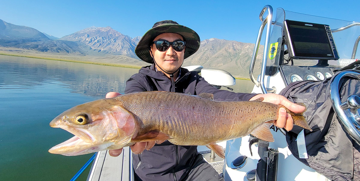 A fly fishermen holding a large cutthroat trout in a boat on Crowley Lake in the Eastern Sierra.