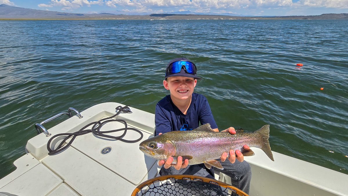 A youngster fly fishermen holding a large rainbow trout in a boat on Crowley Lake in the Eastern Sierra.