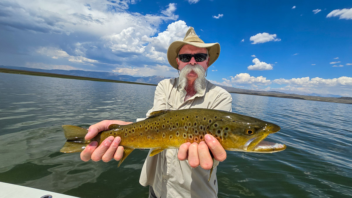 A fly fishermen holding a large brown trout in a boat on Crowley Lake in the Eastern Sierra.