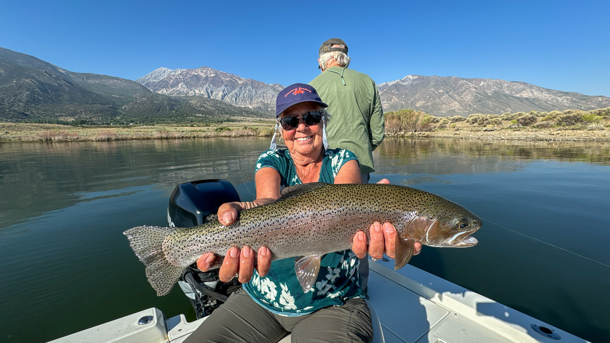 A fly fishermen holding a large rainbow trout in a boat on Crowley Lake in the Eastern Sierra.