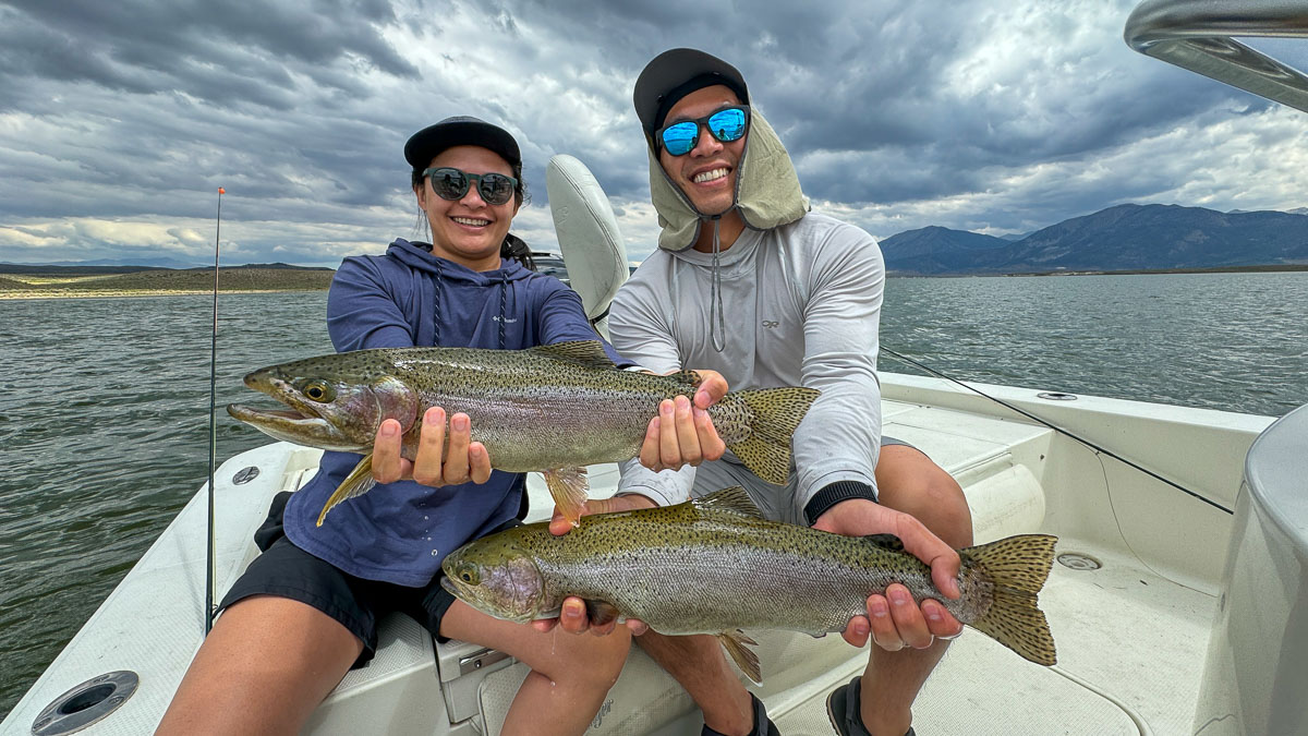 A couple of fly fishermen holding 2 large rainbow trout in a boat on Crowley Lake in the Eastern Sierra.