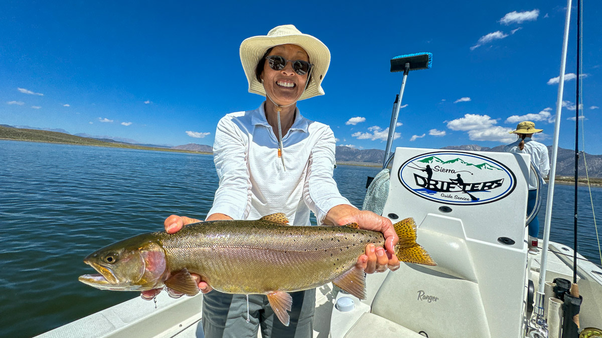 A fly fishermen holding a large cutthroat trout in a boat on Crowley Lake in the Eastern Sierra.