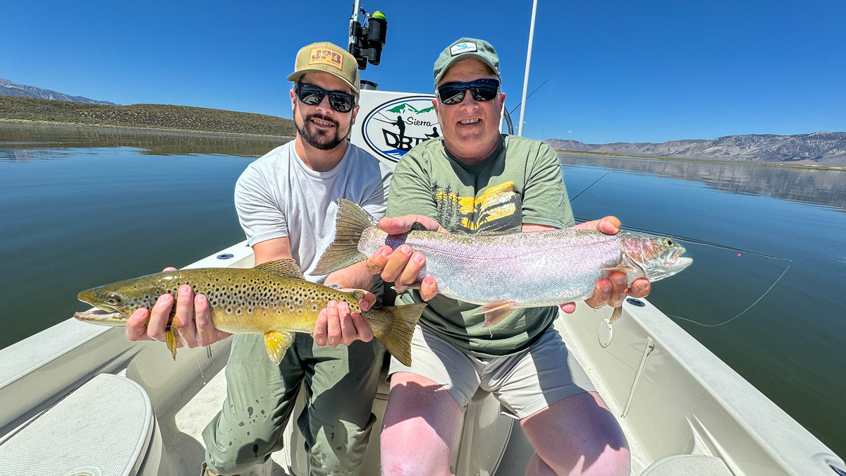 A couple of fly fishermen holding a large rainbow and large brown trout in a boat on Crowley Lake.