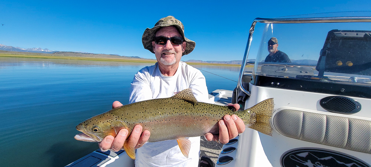 A fly fishermen holding a large rainbow trout in a boat on Crowley Lake in the Eastern Sierra.