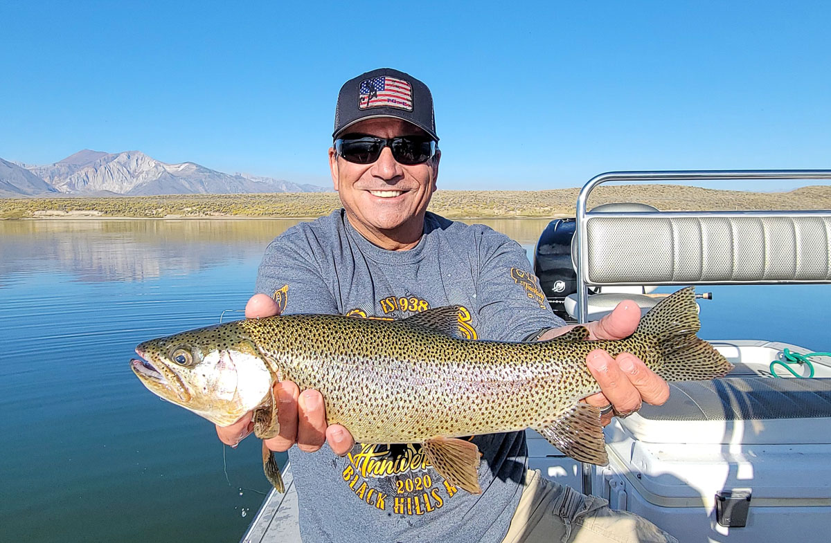 A fly fishermen holding a large rainbow trout in a boat on Crowley Lake in the Eastern Sierra.