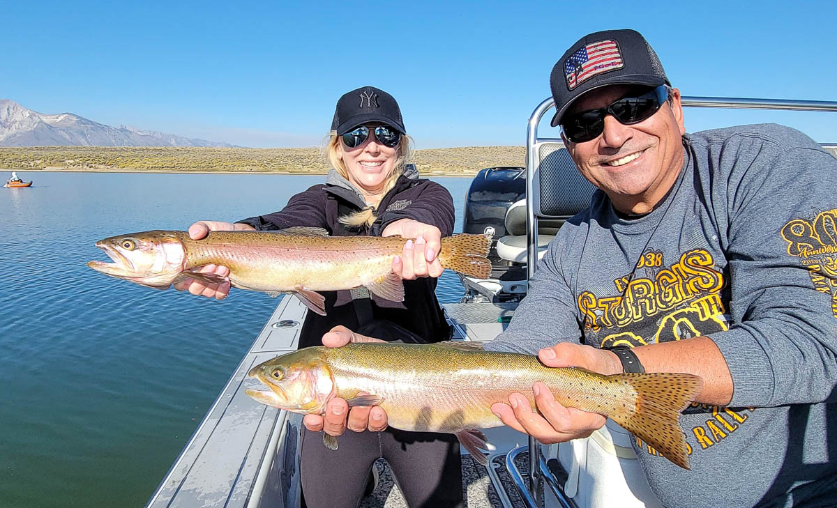 A couple of fly fishermen holding 2 large rainbow trout in a boat on Crowley Lake in the Eastern Sierra.