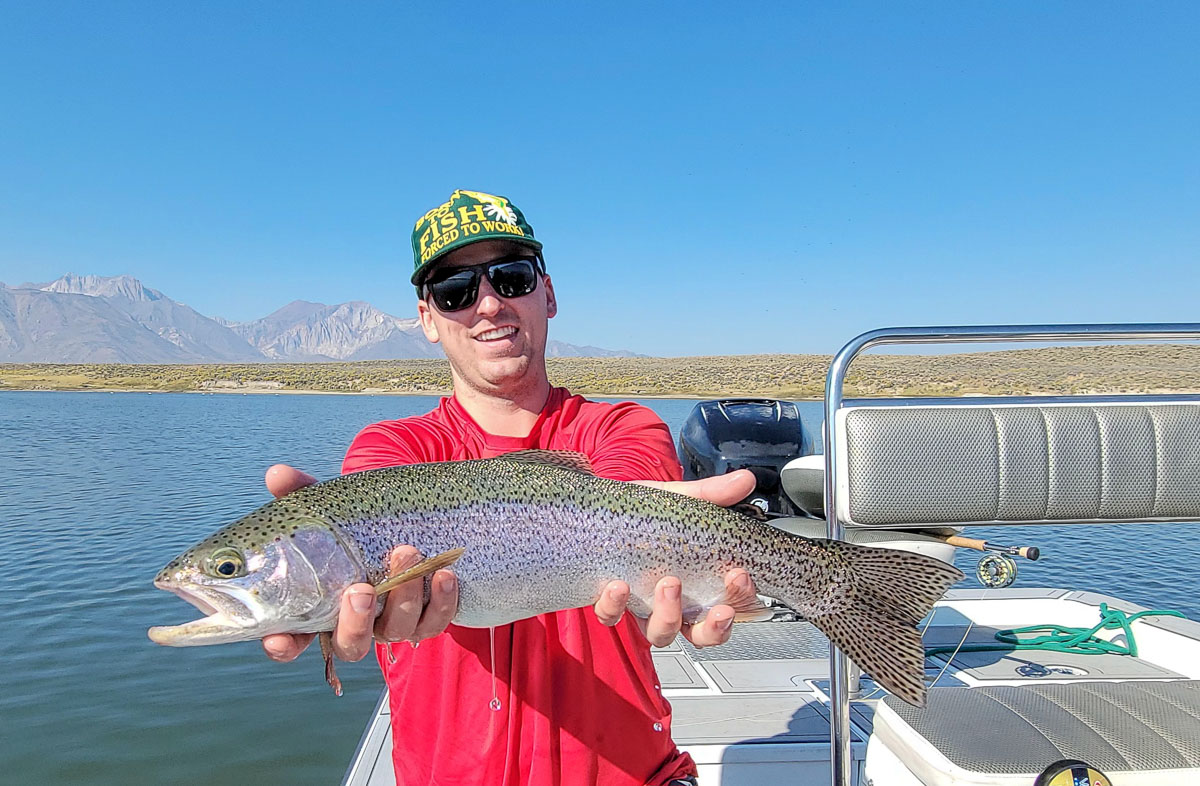 A fly fishermen holding a large rainbow trout in a boat on Crowley Lake in the Eastern Sierra.