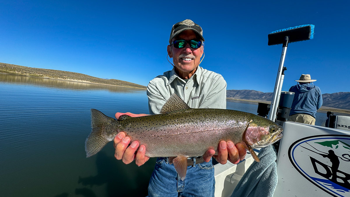 A couple of fly fishermen holding a large rainbow and large brown trout in a boat on Crowley Lake.