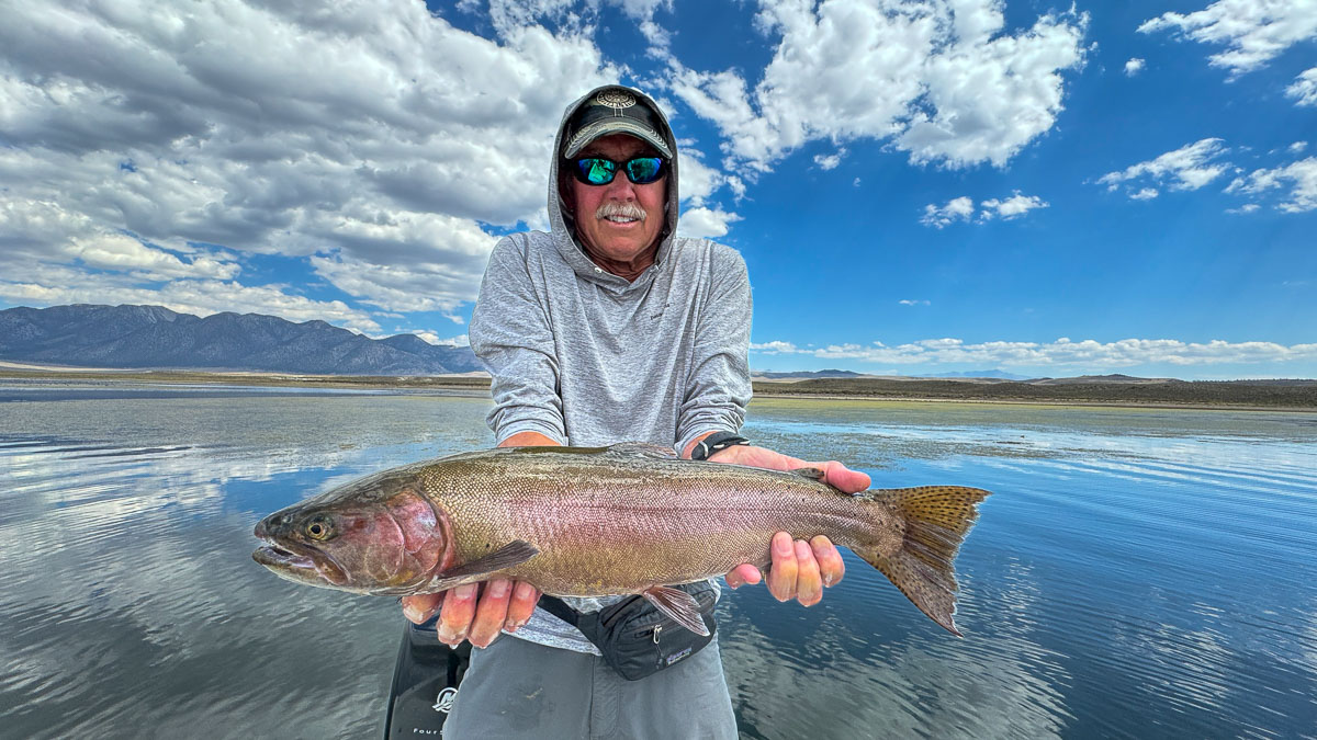 A fly fishermen holding a large cutthroat trout in a boat on Crowley Lake in the Eastern Sierra.