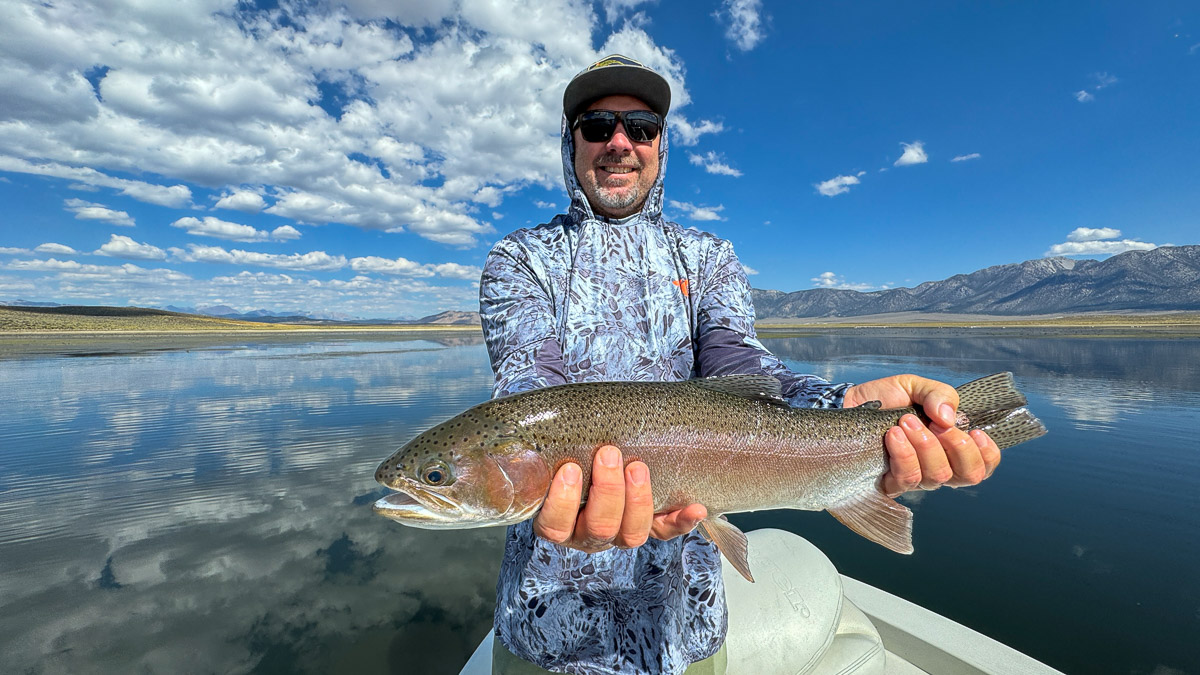 A fly fishermen holding a large rainbow trout in a boat on Crowley Lake in the Eastern Sierra.