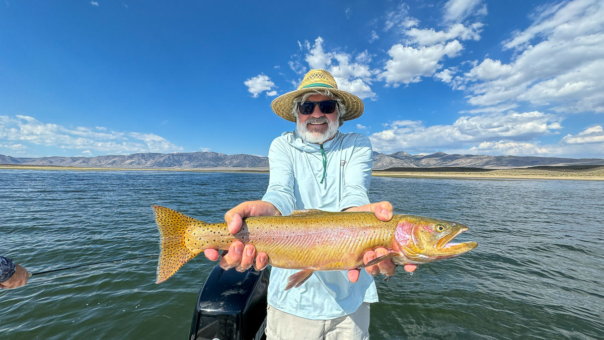 A couple of fly fishermen holding a large rainbow and large brown trout in a boat on Crowley Lake.