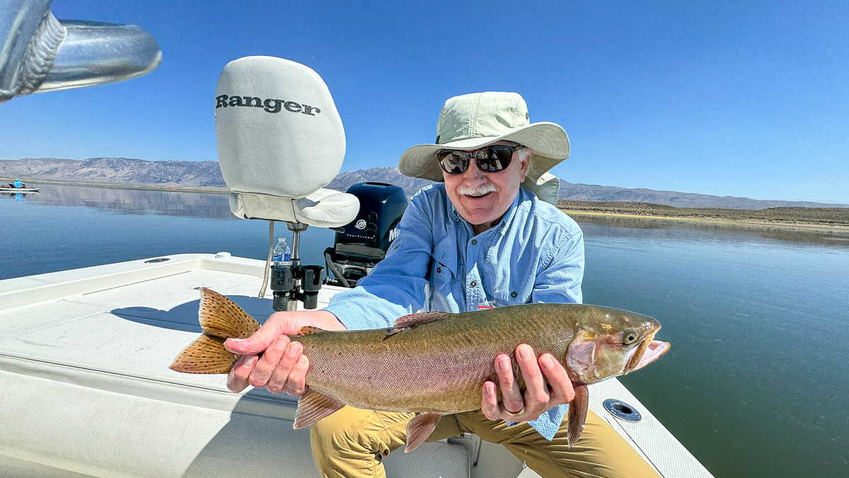 A fly fishermen holding a large rainbow trout in a boat on Crowley Lake in the Eastern Sierra.