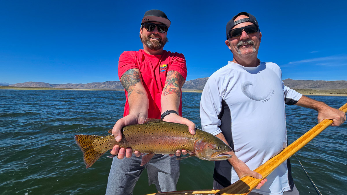 A fly fishermen holding a large cutthroat trout in a boat on Crowley Lake in the Eastern Sierra.