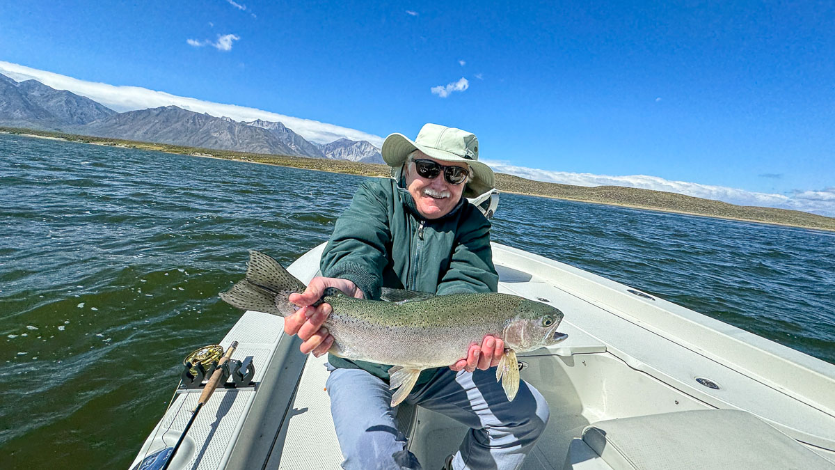 A fly fishermen holding a large rainbow trout in a boat on Crowley Lake in the Eastern Sierra.