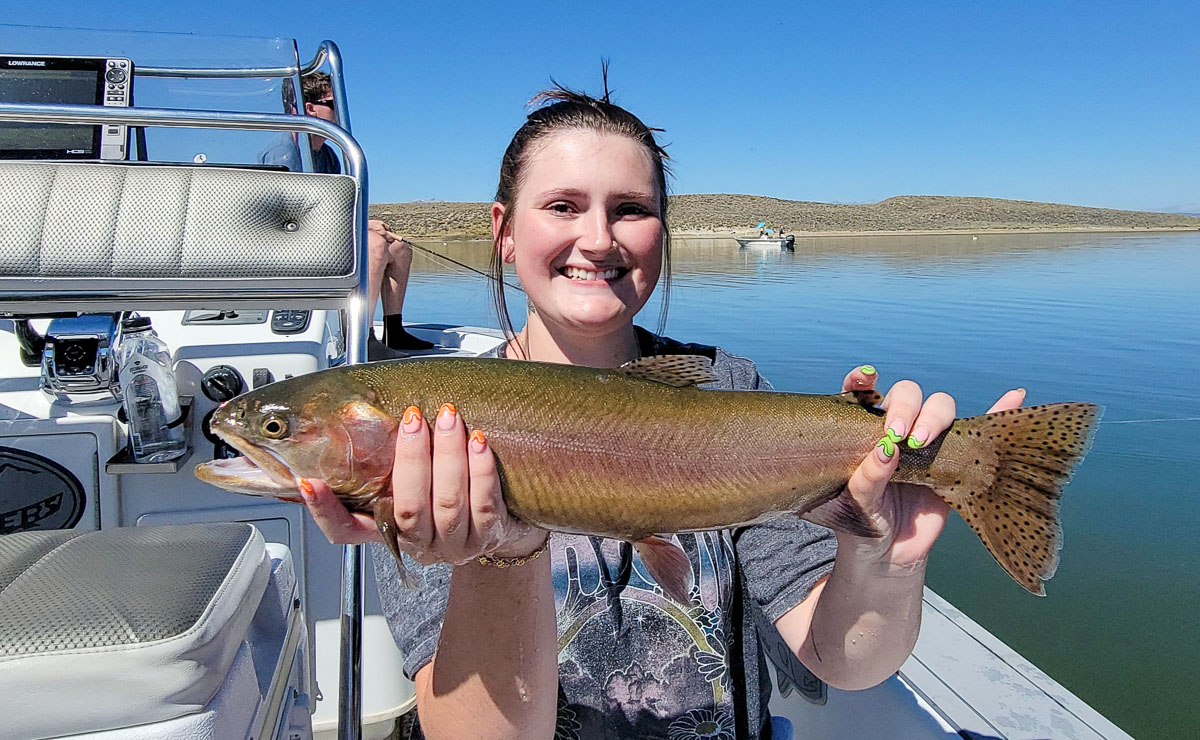 A fly fishermen holding a large cutthroat trout in a boat on Crowley Lake in the Eastern Sierra.