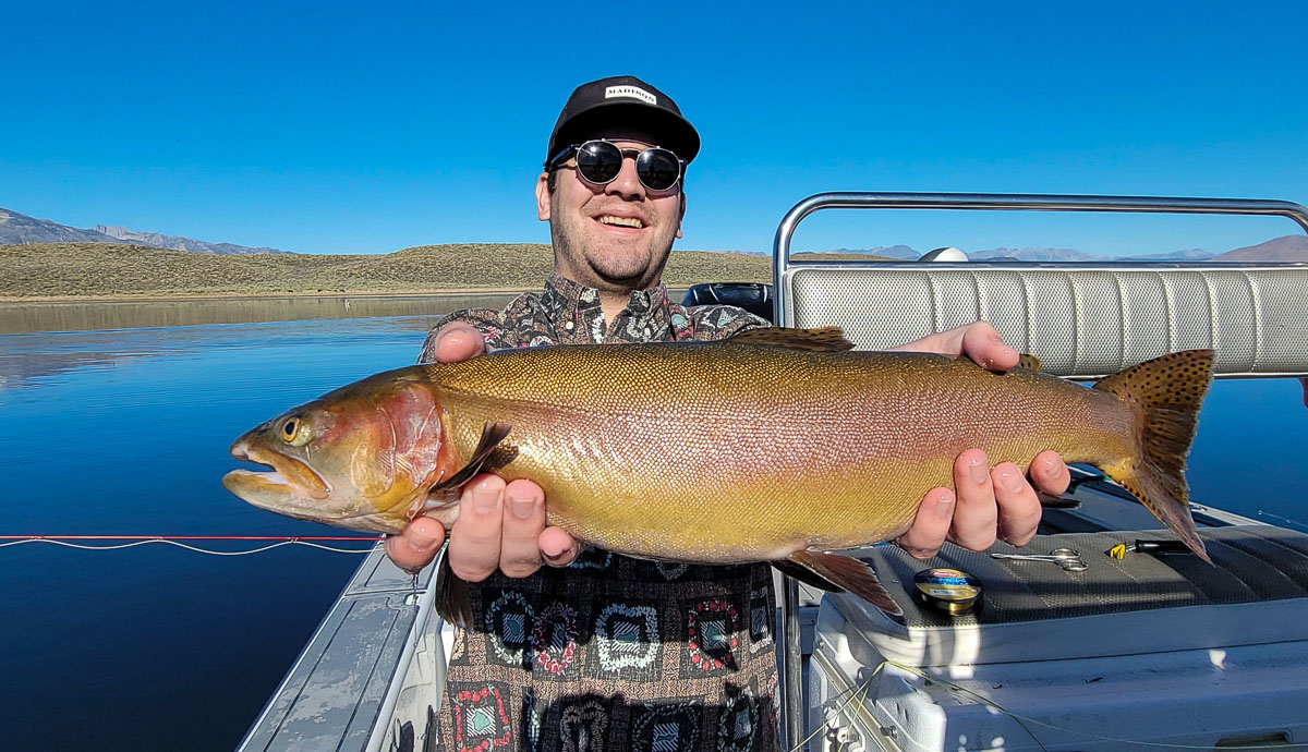 A fly fishermen holding a large brown trout in a boat on Crowley Lake in the Eastern Sierra.