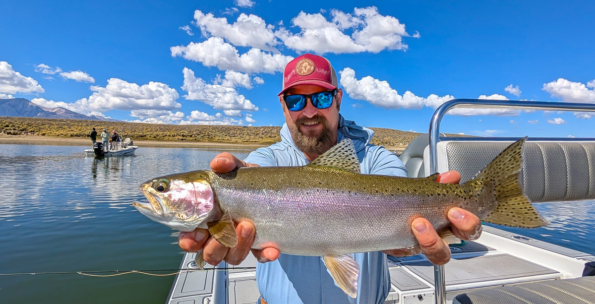 A fly fishermen holding a large cutthroat trout in a boat on Crowley Lake in the Eastern Sierra.