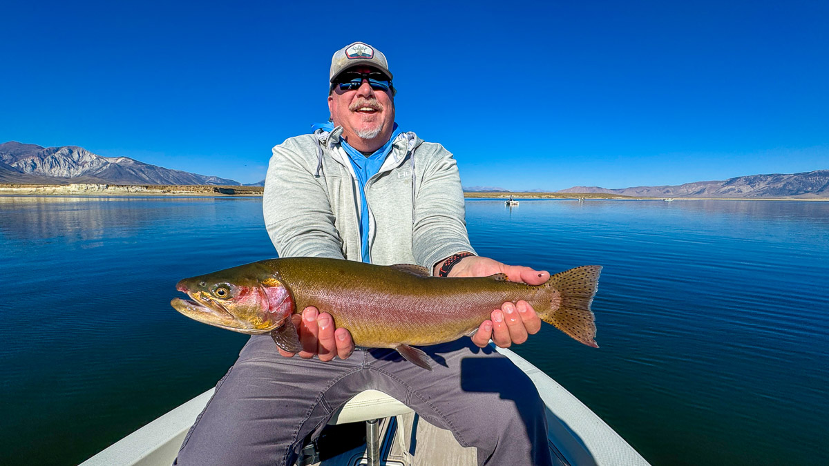 A couple of fly fishermen holding a large rainbow and large brown trout in a boat on Crowley Lake.