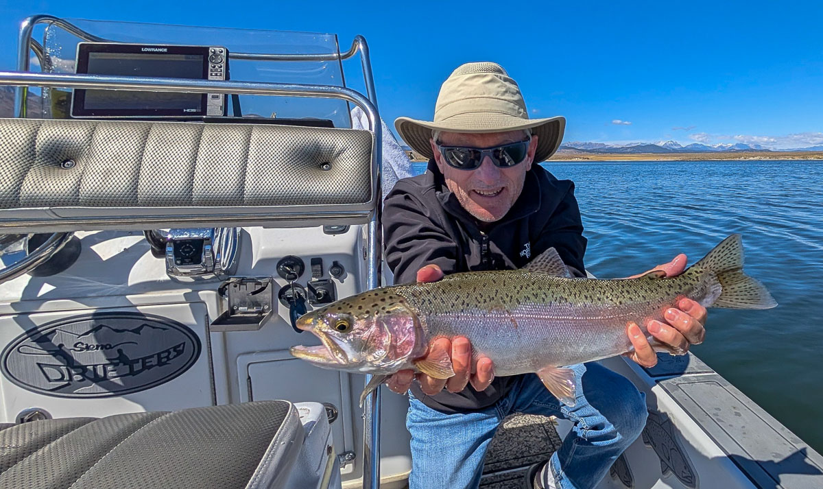 A fly fishermen holding a large rainbow trout in a boat on Crowley Lake in the Eastern Sierra.