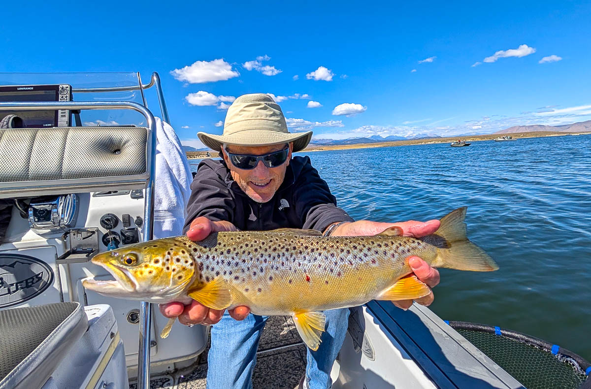 A fly fishermen holding a large rainbow trout in a boat on Crowley Lake in the Eastern Sierra.