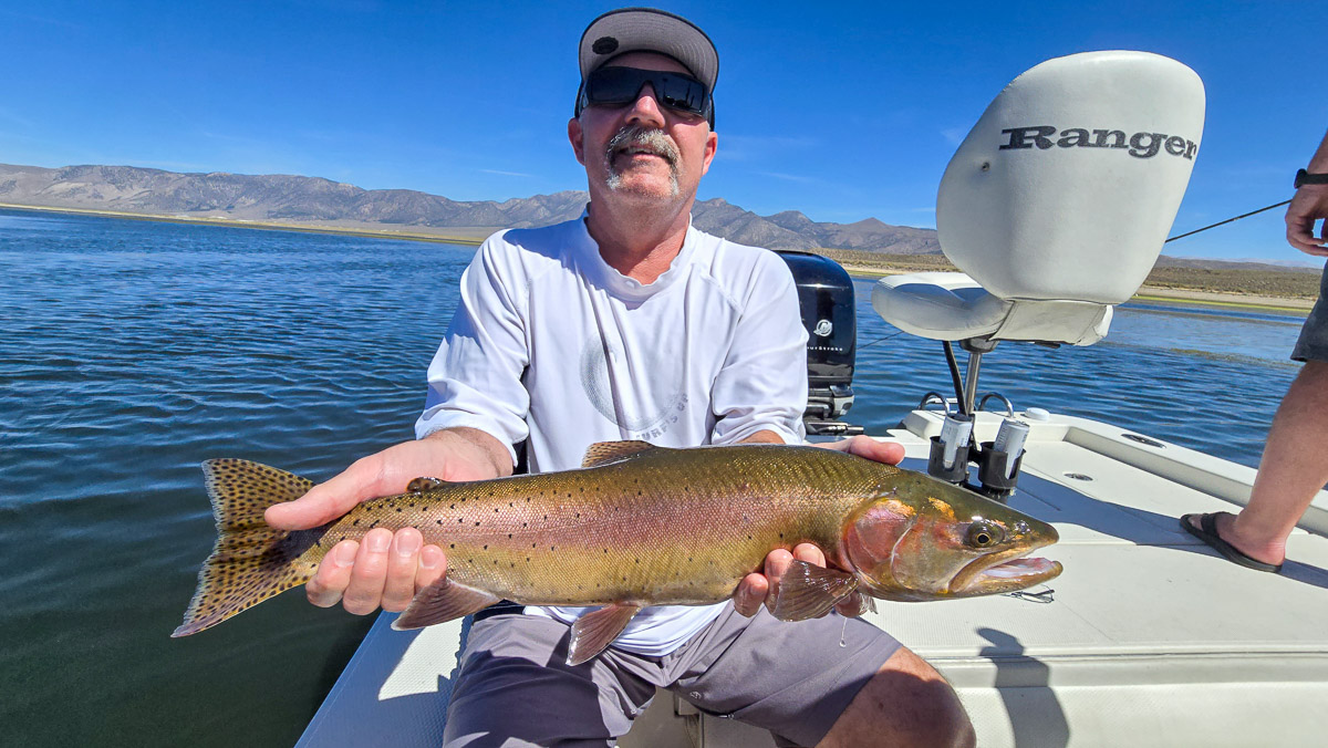 A fly fishermen holding a large brown trout in a boat on Crowley Lake in the Eastern Sierra.