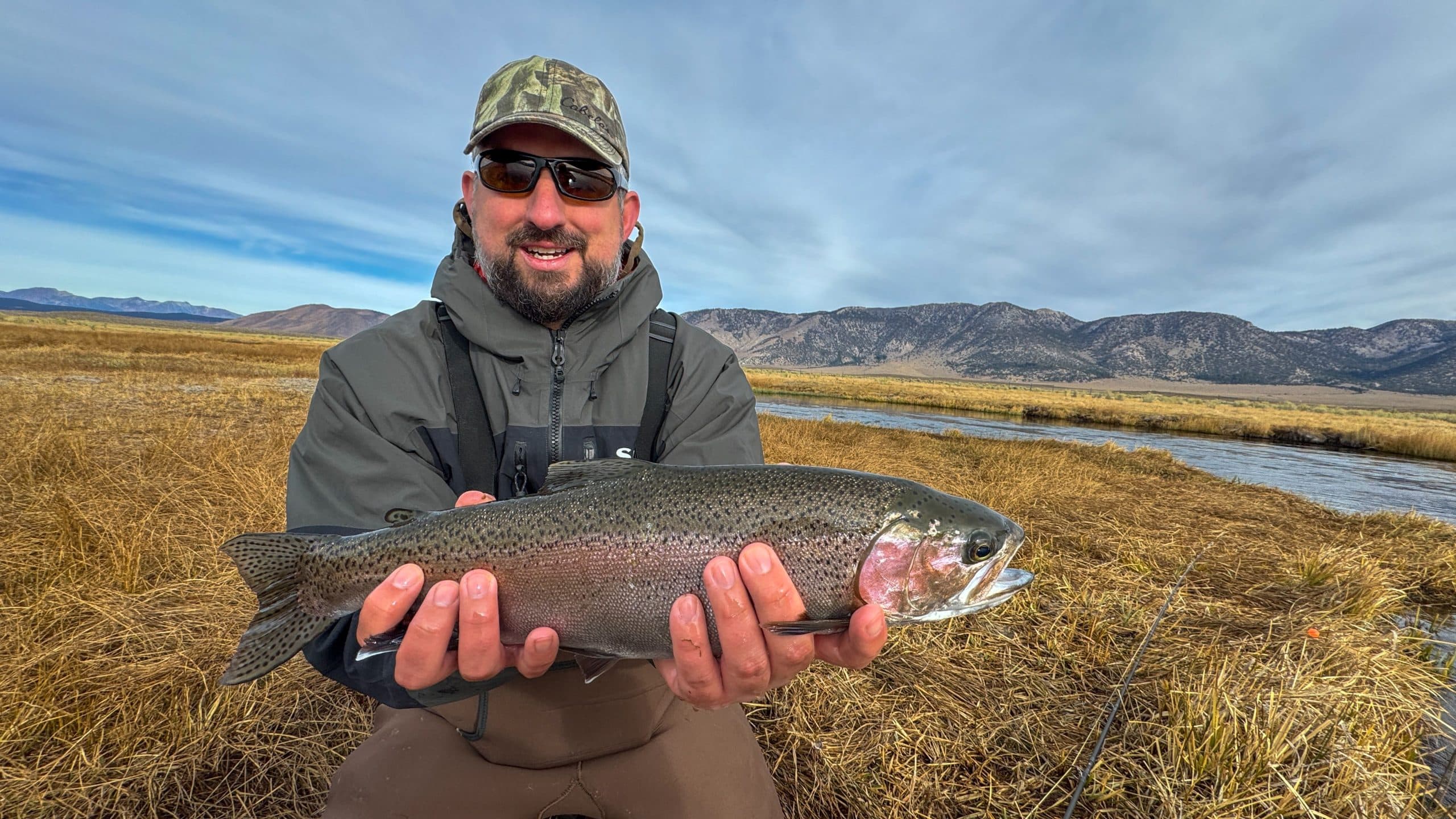 A smiling fly fisherman holding a larger rainbow trout on the Upper Owens River near Mammoth Lakes, CA.