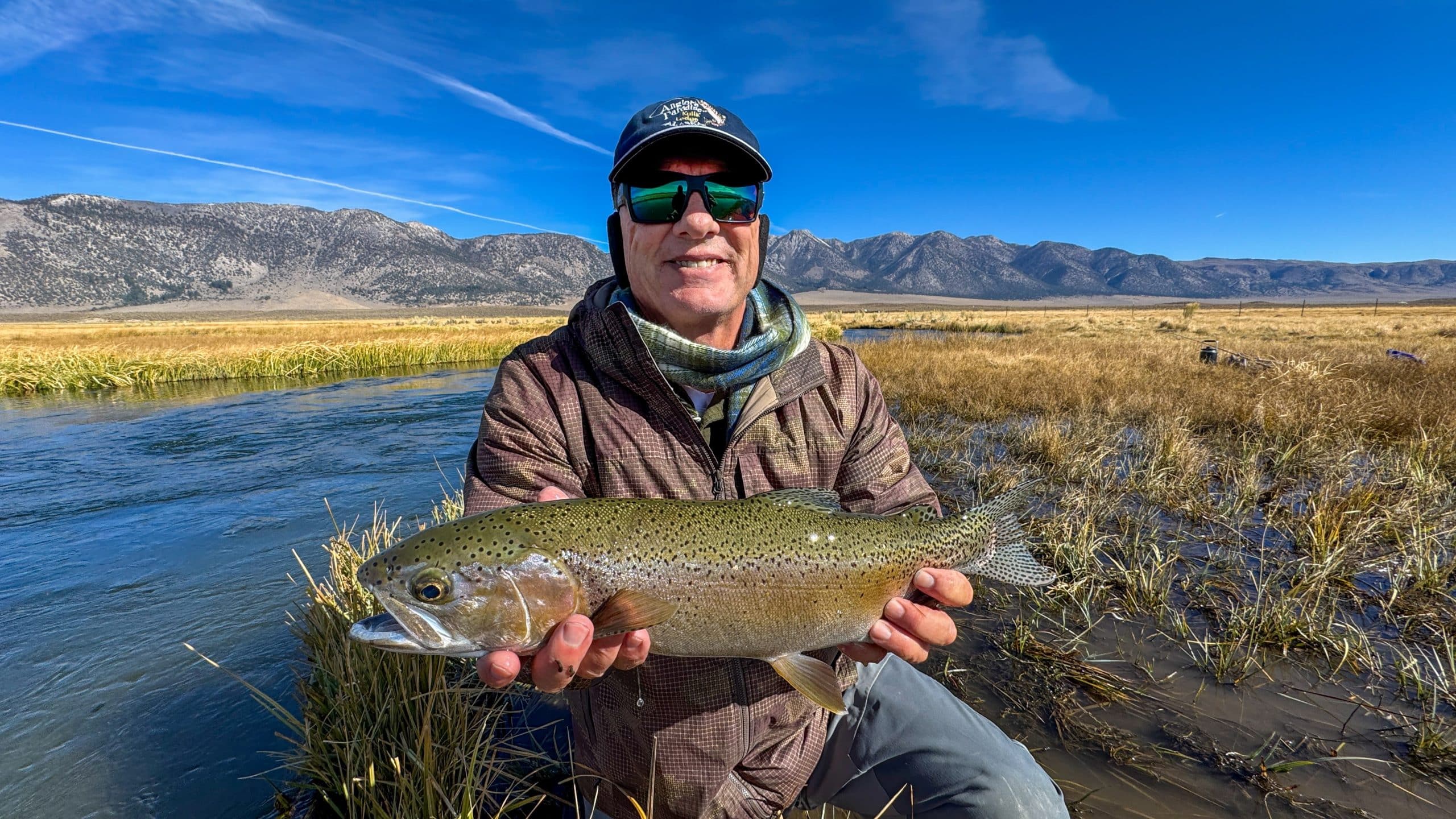 A smiling fly fisherman holding a larger rainbow trout on the Upper Owens River near Mammoth Lakes, CA.