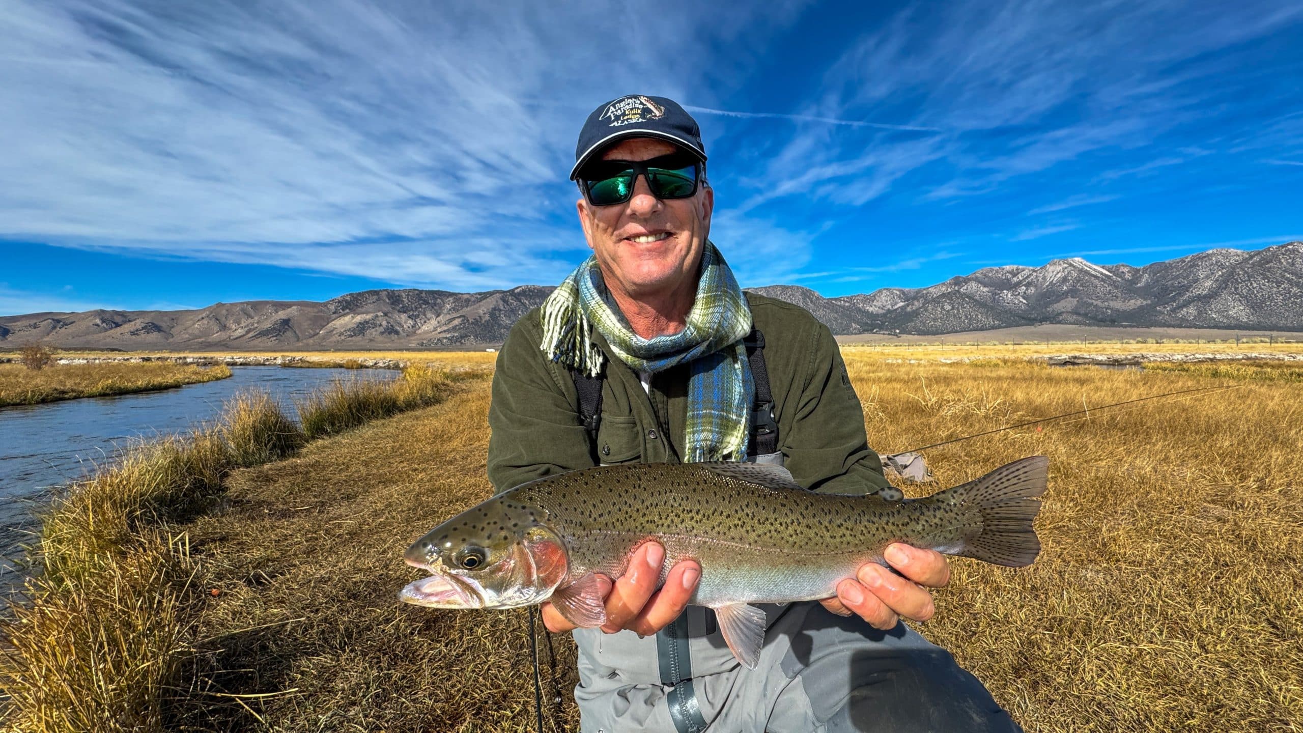 A smiling fly fisherman holding a larger rainbow trout on the Upper Owens River near Mammoth Lakes, CA.