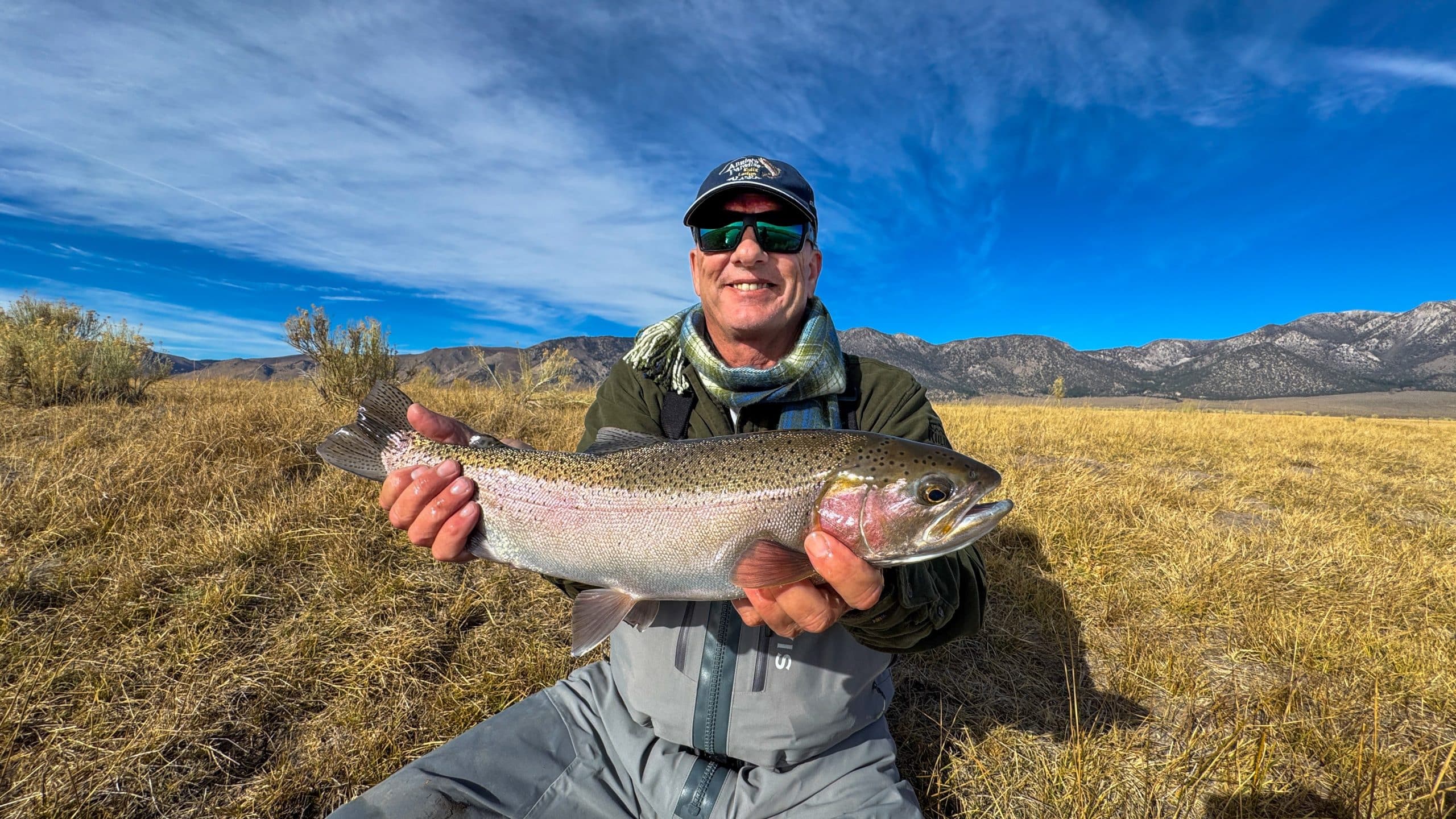 A smiling fly fisherman holding a larger rainbow trout on the Upper Owens River near Mammoth Lakes, CA.