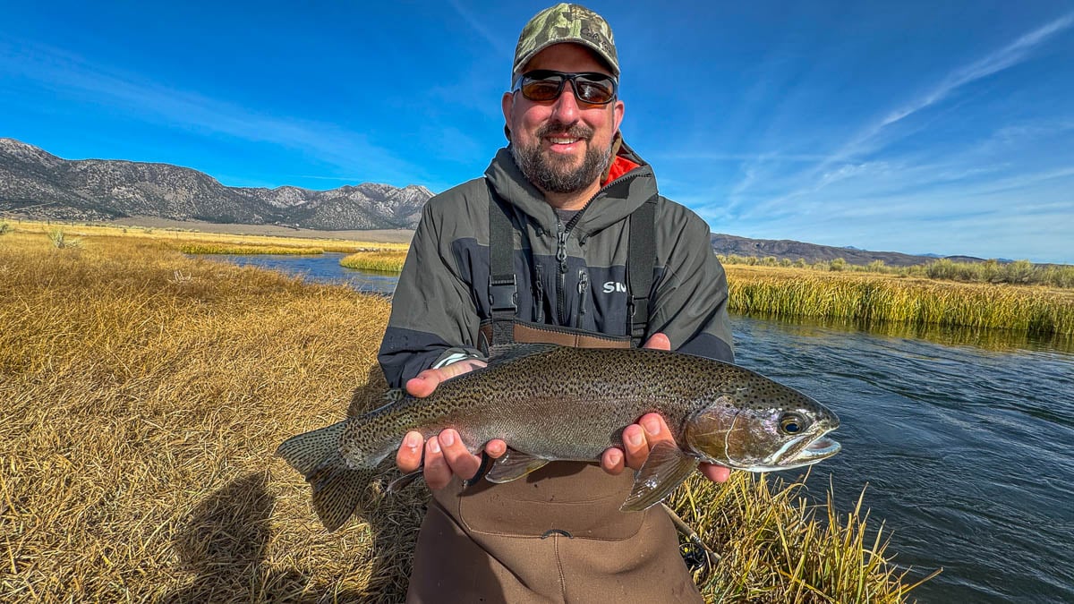 A smiling fly fisherman holding a larger rainbow trout on the Upper Owens River near Mammoth Lakes, CA.