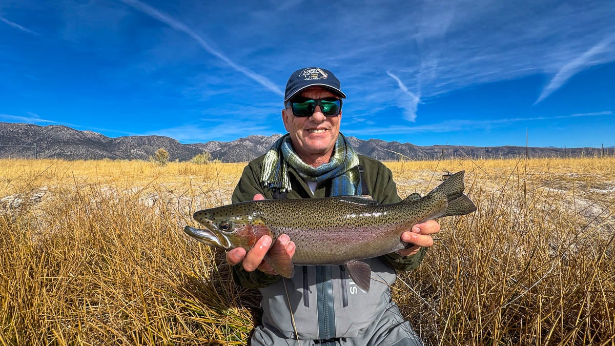 A smiling fly fisherman holding a larger rainbow trout on the Upper Owens River near Mammoth Lakes, CA.