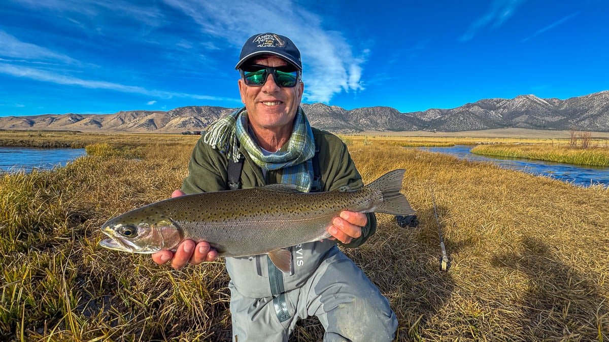 A smiling fly fisherman holding a larger rainbow trout on the Upper Owens River near Mammoth Lakes, CA.