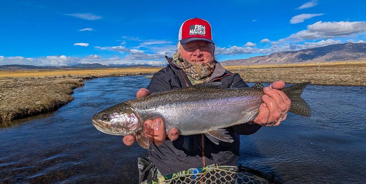 A smiling fly fisherman holding a larger rainbow trout on the Upper Owens River near Mammoth Lakes, CA.