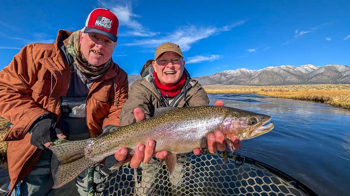 A smiling fly fisherman holding a larger rainbow trout on the Upper Owens River near Mammoth Lakes, CA.