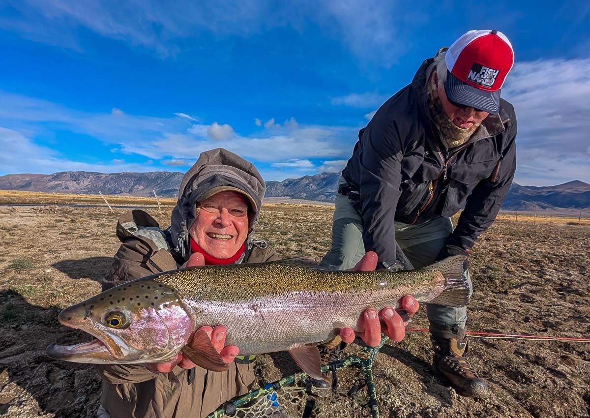 A smiling fly fisherman holding a larger rainbow trout on the Upper Owens River near Mammoth Lakes, CA.