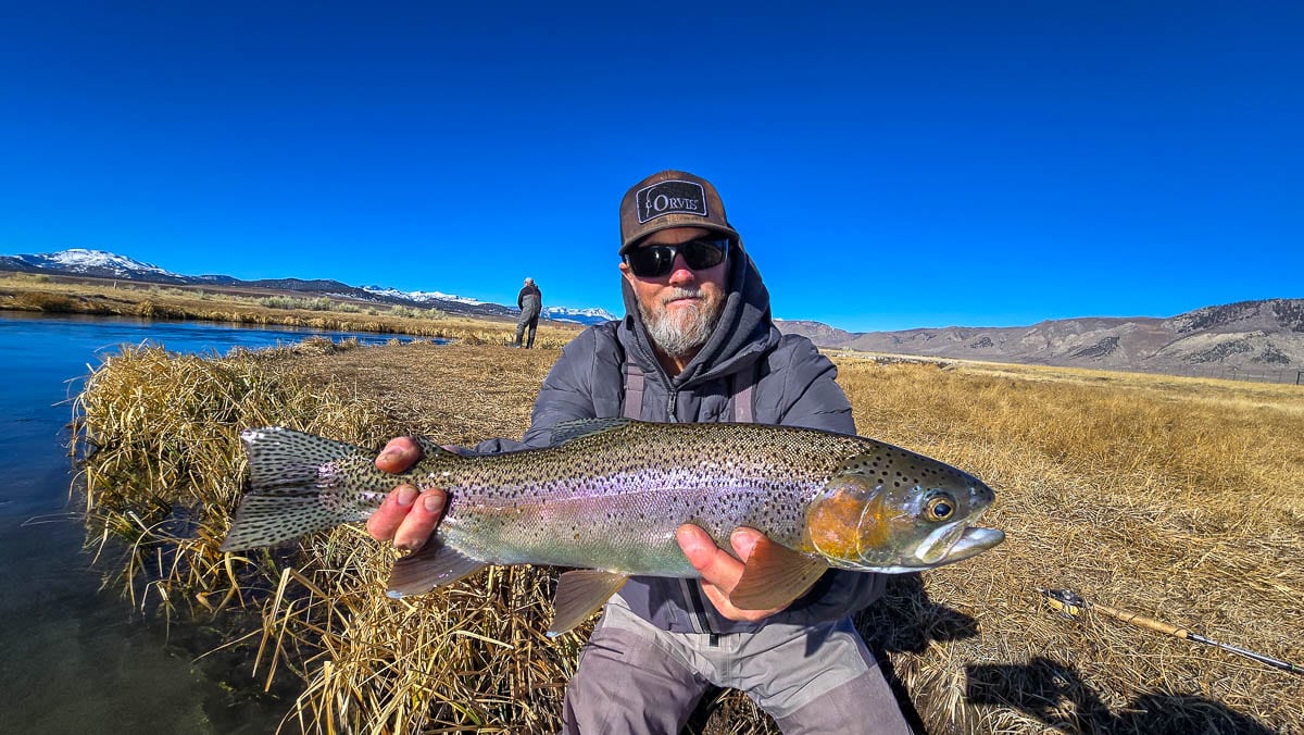 A smiling fly fisherman holding a larger rainbow trout on the Upper Owens River near Mammoth Lakes, CA.