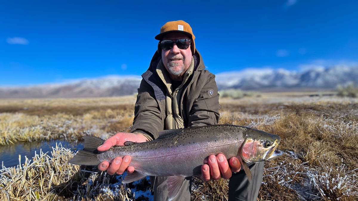 A smiling fly fisherman holding a larger rainbow trout on the Upper Owens River near Mammoth Lakes, CA.