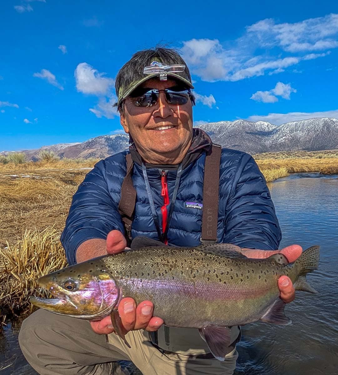 A smiling fly fishermen holding a giant rainbow trout on the Upper Owens River near Mammoth Lakes, CA