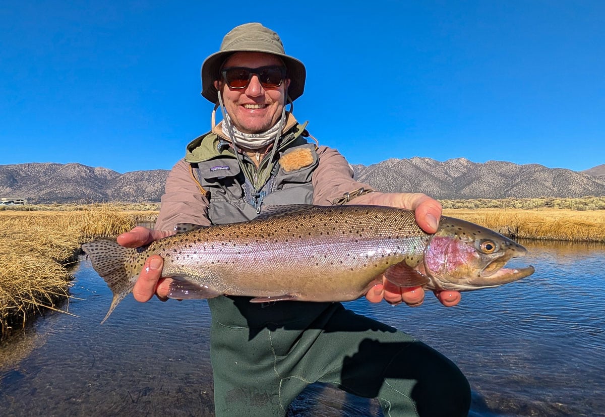 A smiling fly fisherman holding a larger rainbow trout on the Upper Owens River near Mammoth Lakes, CA.