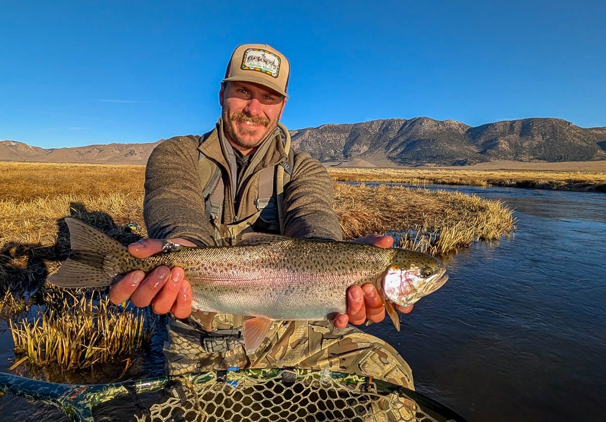 A smiling fly fisherman holding a larger rainbow trout on the Upper Owens River near Mammoth Lakes, CA.