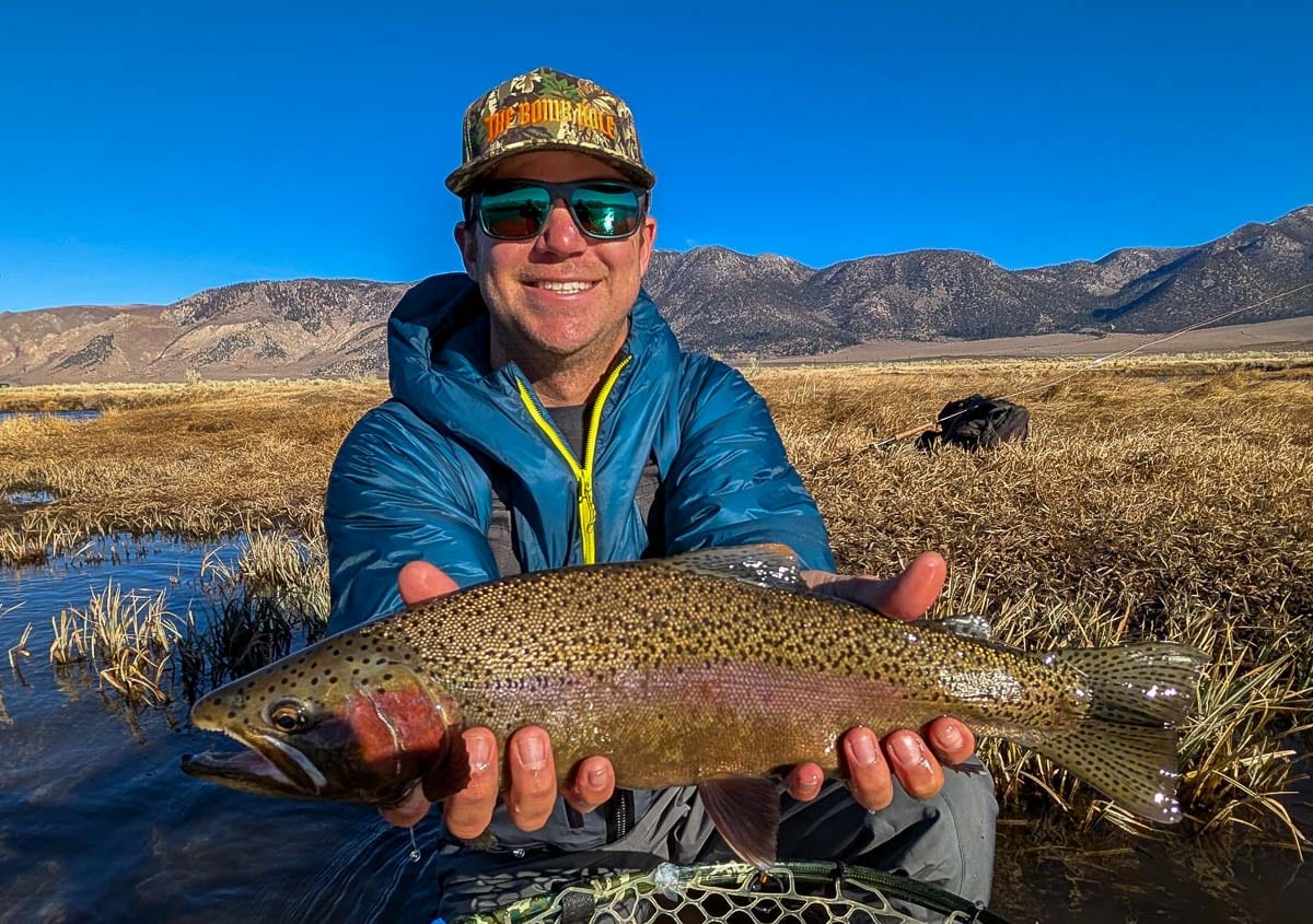 A smiling fly fisherman holding a larger rainbow trout on the Upper Owens River near Mammoth Lakes, CA.