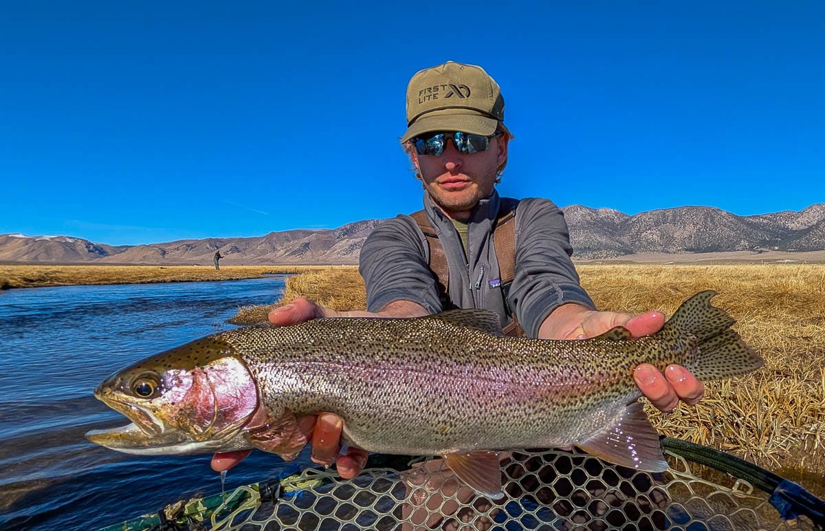 A smiling fly fisherman holding a larger rainbow trout on the Upper Owens River near Mammoth Lakes, CA.